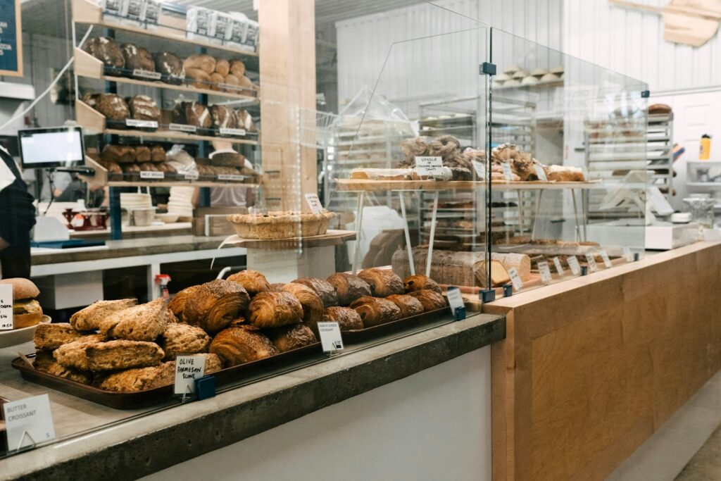 Bakery counter with a register screen, trays of scones and croissants, and a pie on a stand behind glass