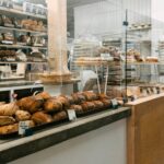 Bakery counter with a register screen, trays of scones and croissants, and a pie on a stand behind glass