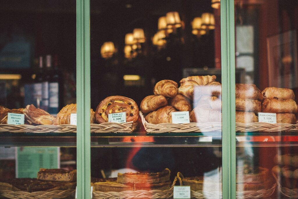 Croissants and pastries in wicker baskets with small price cards, seen through a bakery window