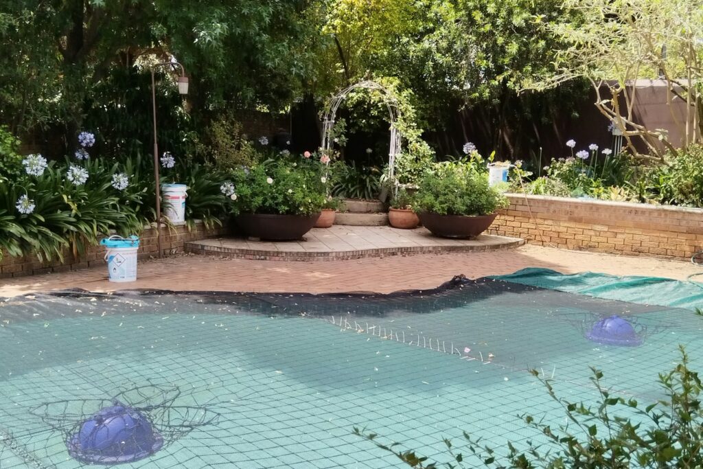 Backyard swimming pool under a green mesh safety cover with floating chlorinators, closed for the off-season