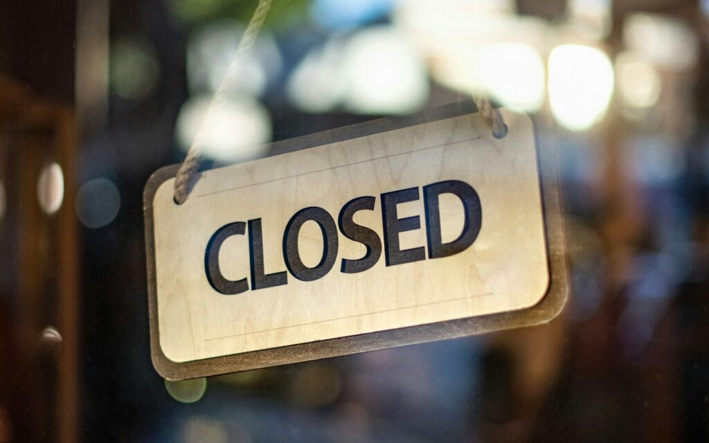 Wooden CLOSED sign hanging by a rope inside a glass shop door, a reminder to set holiday hours