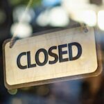 Wooden CLOSED sign hanging by a rope inside a glass shop door, a reminder to set holiday hours